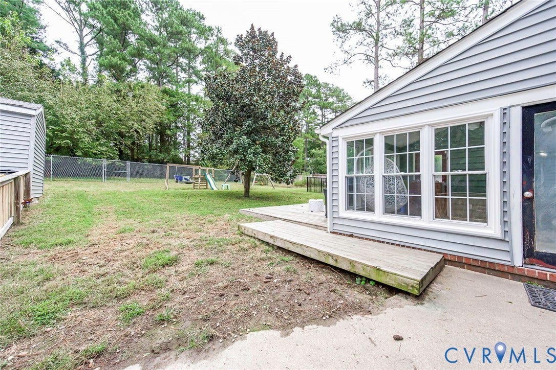 5640 Teterling Court, Lakewood Farms, Chester, VA 23831 Rear exterior featuring light gray siding, a wood deck, a concrete patio, and a chain-link fence enclosing the yard