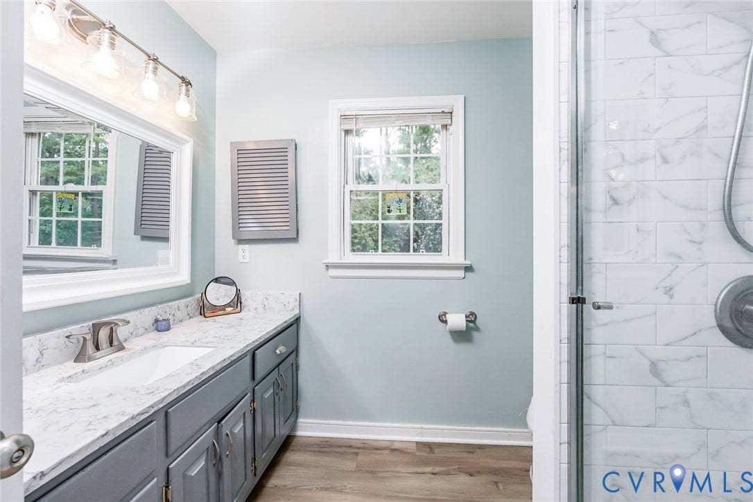 5640 Teterling Court, Lakewood Farms, Chester, VA 23831 Vanity with integrated sink and chrome faucet, framed mirror with vanity lighting, window with white trim, wood-finish flooring, and a tiled shower with glass enclosure