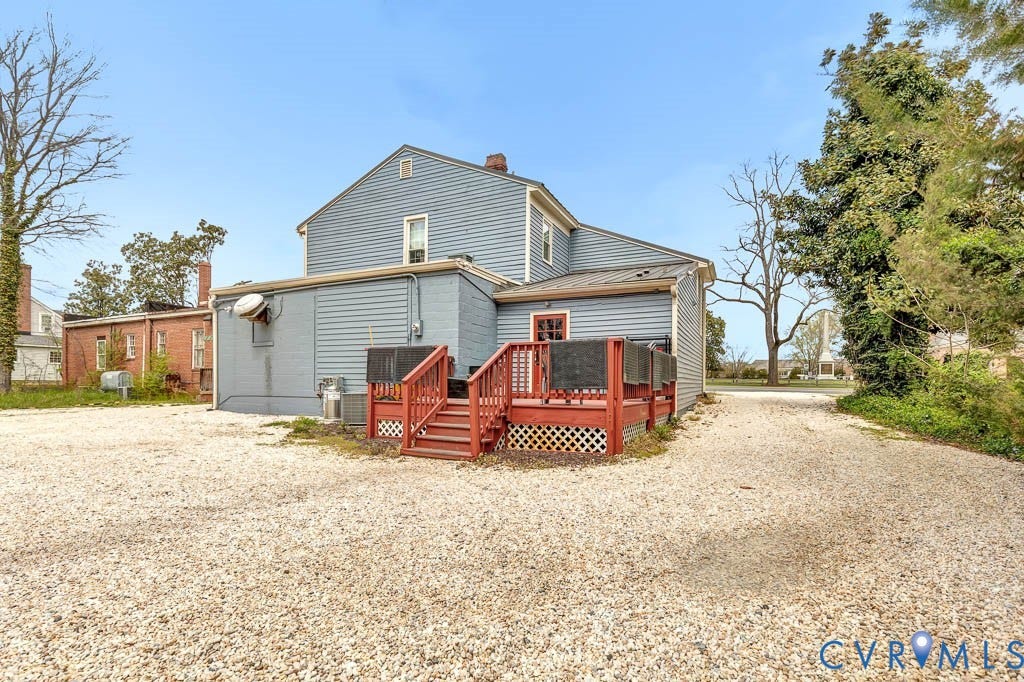 Side exterior featuring blue siding, a red-painted wood deck, and a gravel surface