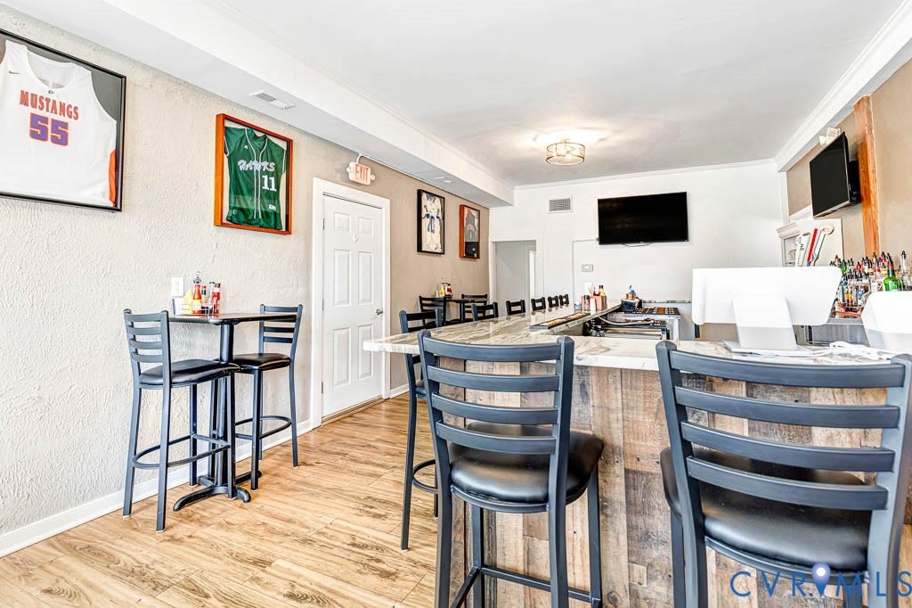 Open bar area featuring wood-finish flooring, a textured accent wall, and a built-in bar with a stone-finish countertop