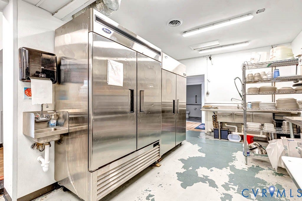 Commercial-grade kitchen space featuring multiple stainless steel refrigerators, a handwashing station, and a triple basin sink