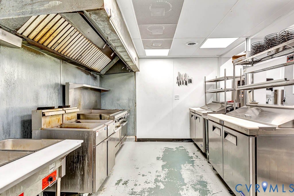 Commercial-grade kitchen featuring stainless steel appliances, extensive counter space, and a large ventilation hood system