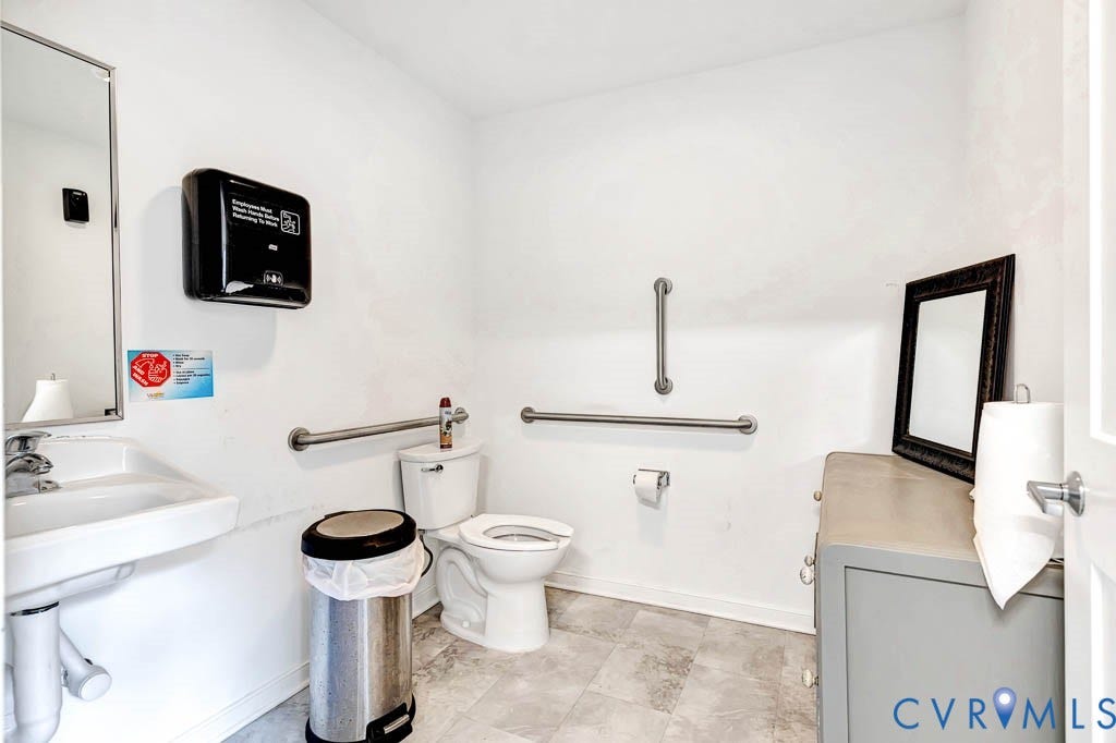 White wall paint, wall-mounted sink, toilet, gray tile flooring, and grab bars