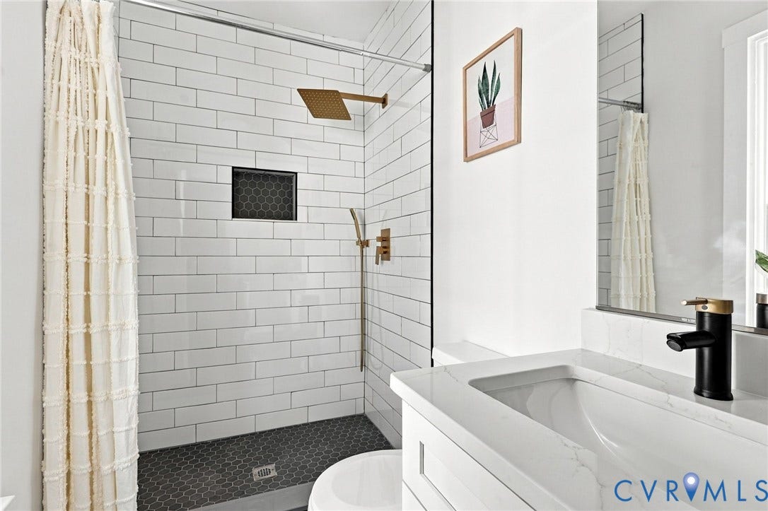 Walk-in shower with white subway tile, a recessed niche with dark hexagonal tile, and a metallic finish rainfall showerhead