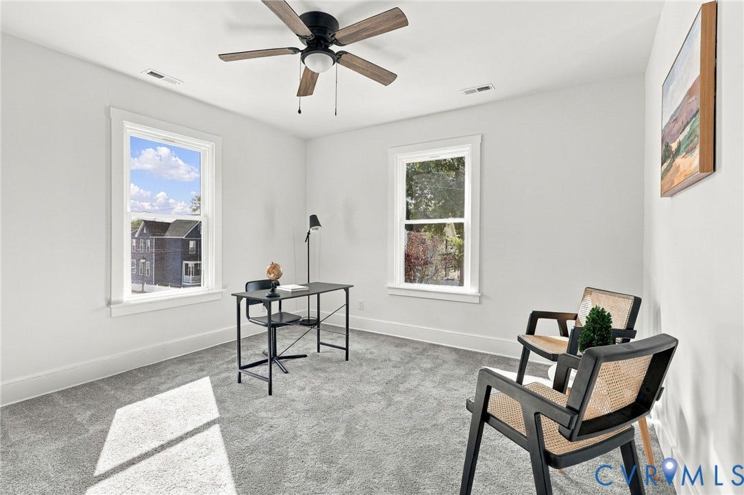Neutral-toned wall finish, plush carpeting, dual double-hung windows, and a ceiling-mounted fan with wood-finish blades