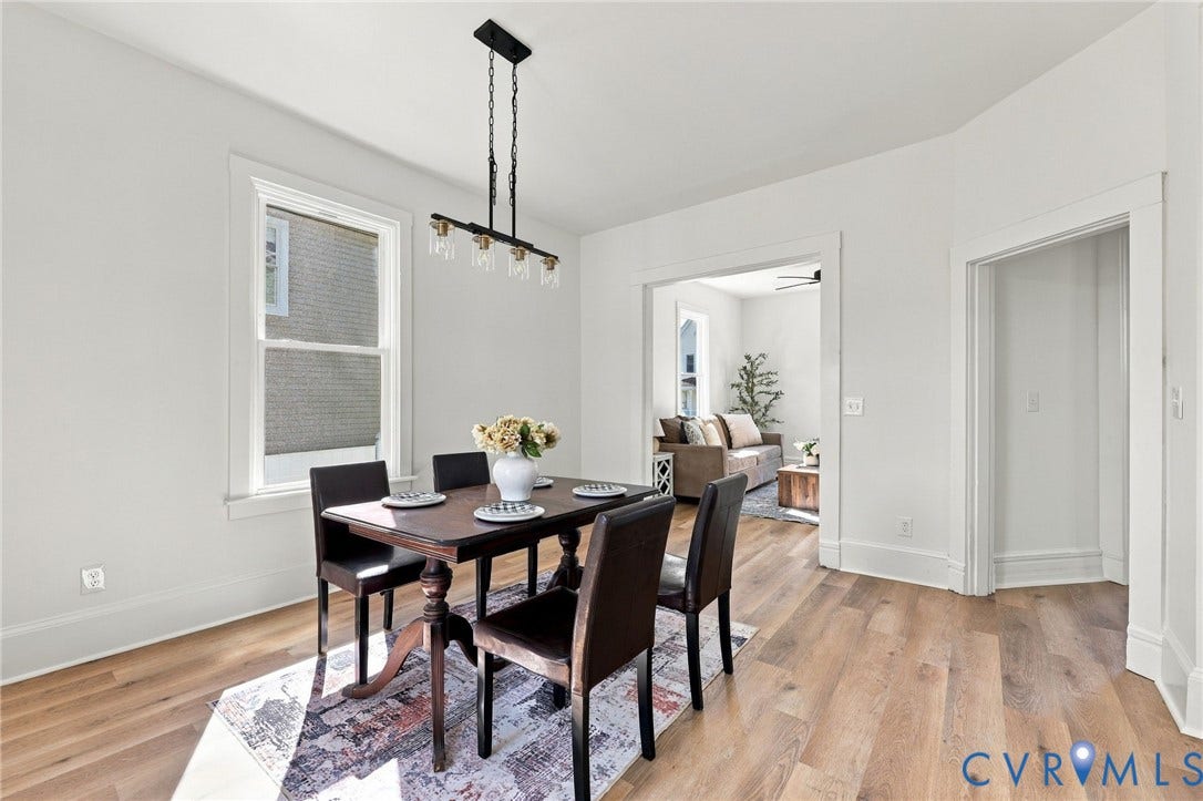Dining space featuring wood-finish flooring, white walls, and a linear black metal pendant light with glass shades