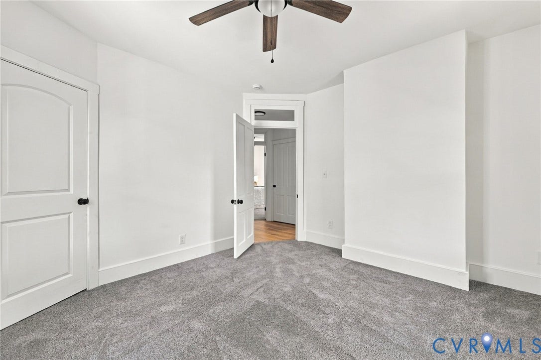 Neutral-toned carpeting, ceiling-mounted paddle fan, and solid-core interior doors with matte black hardware