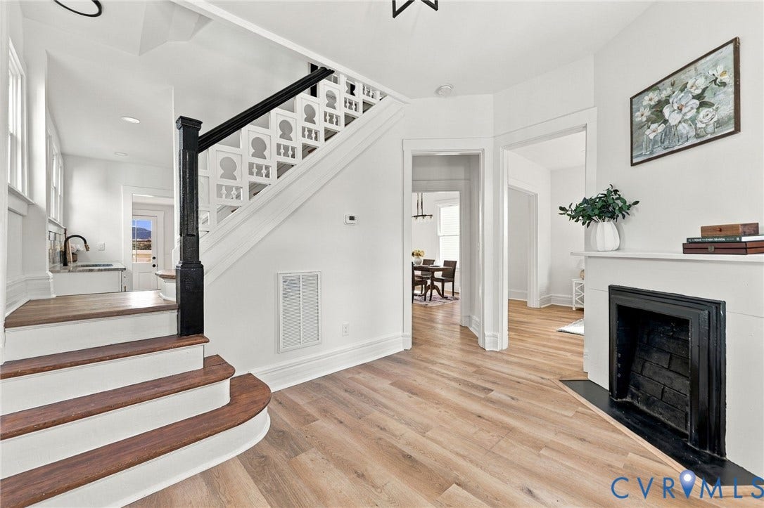 Foyer featuring wood-finish flooring, a fireplace with a black surround, and a staircase with a decorative lattice balustrade and black newel post
