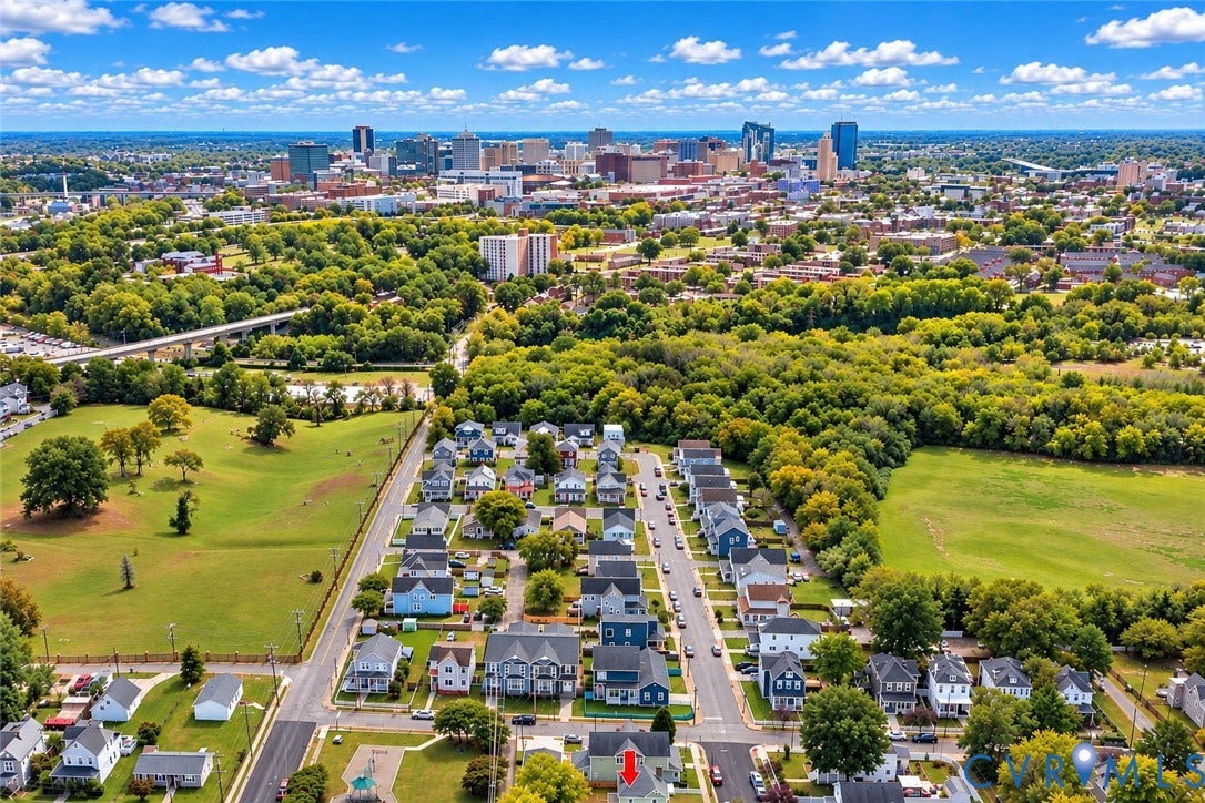 Aerial perspective featuring a residential lot with a gabled roof structure, paved street access, and expansive green space