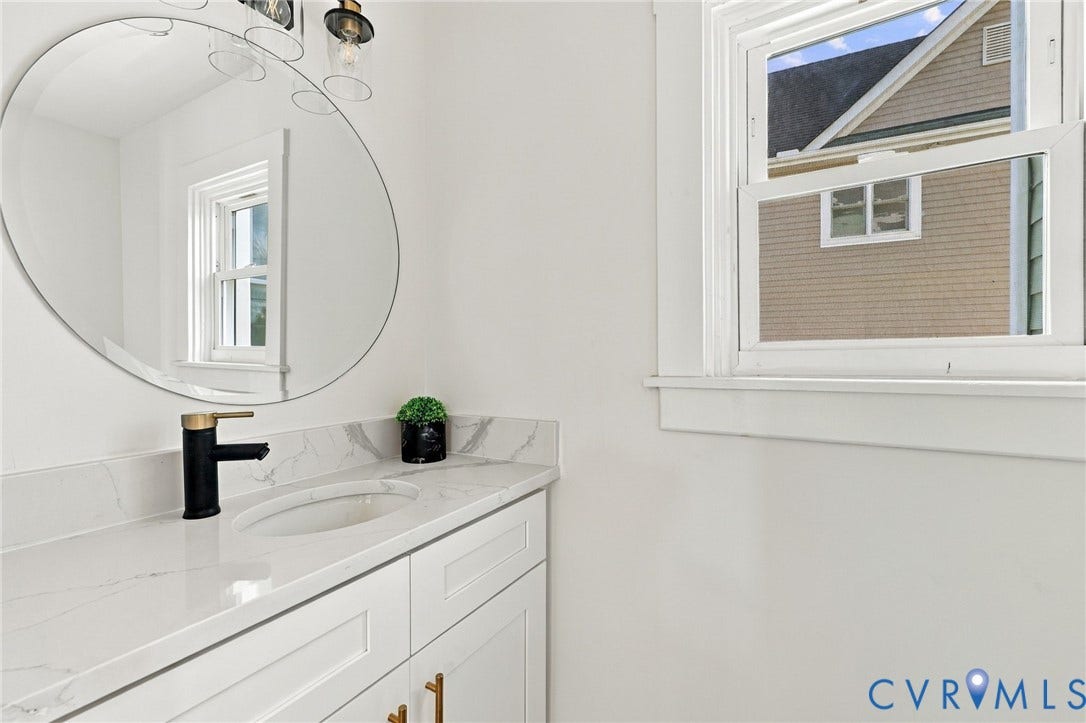 Shaker-style vanity featuring a stone-look countertop, integrated oval basin, modern matte black faucet, and large circular mirror