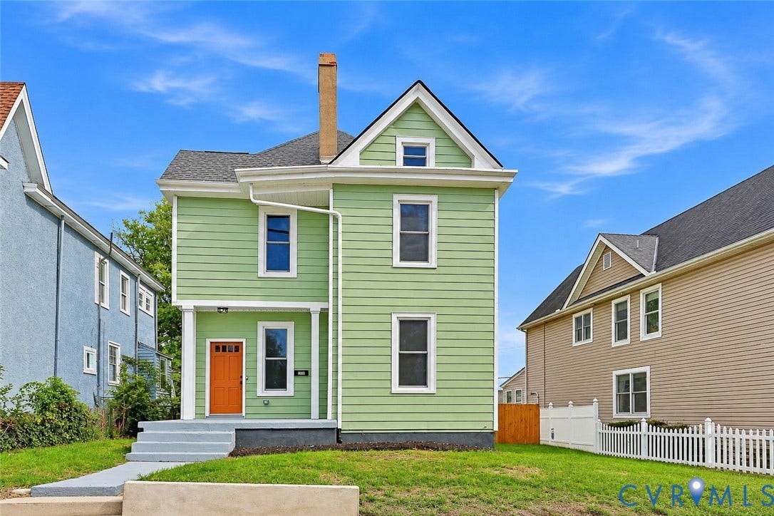 Two-story residence featuring light green horizontal siding, a gabled roofline, a tall masonry chimney, a covered front porch, and a bold orange entry door