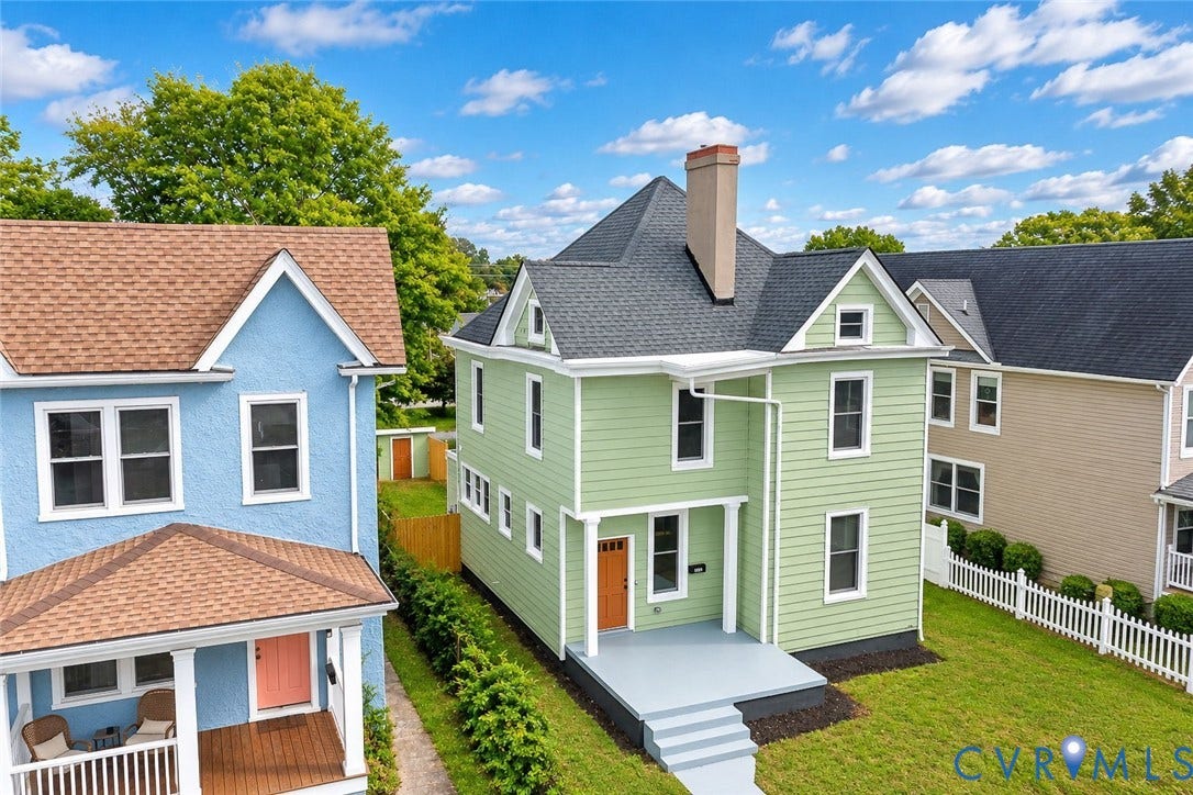 Two-story exterior featuring light green siding, a covered front porch with white columns, a steep gabled roofline, and an exterior chimney