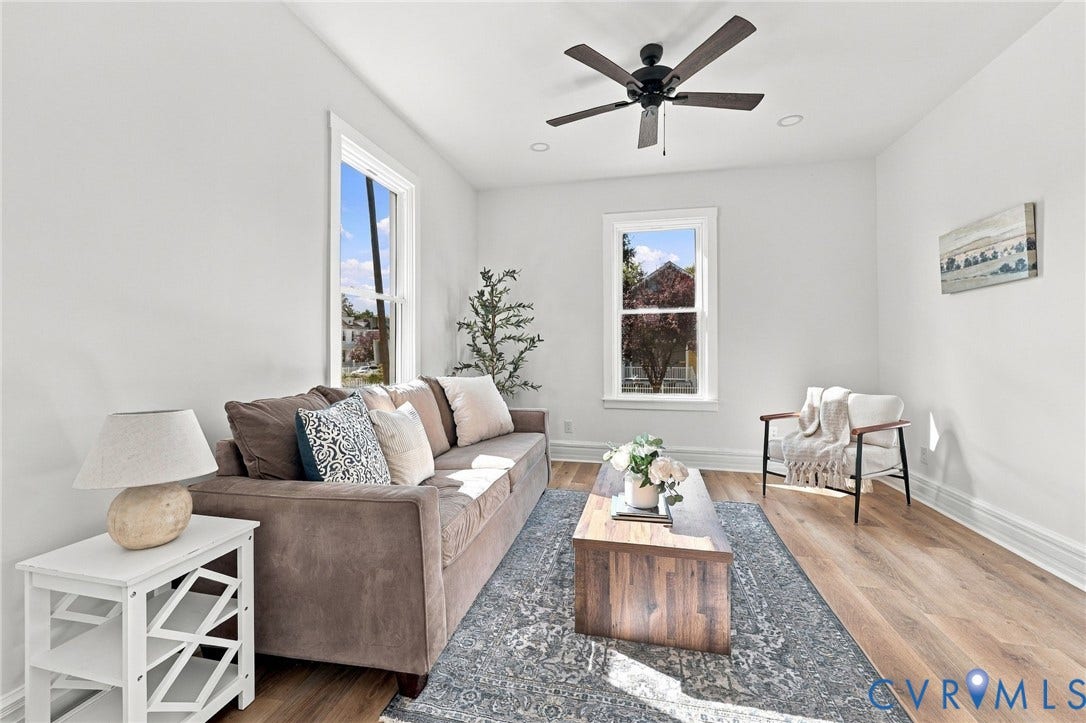 Living area featuring wood-finish flooring, two double-hung windows, and a ceiling fan with matte black finish