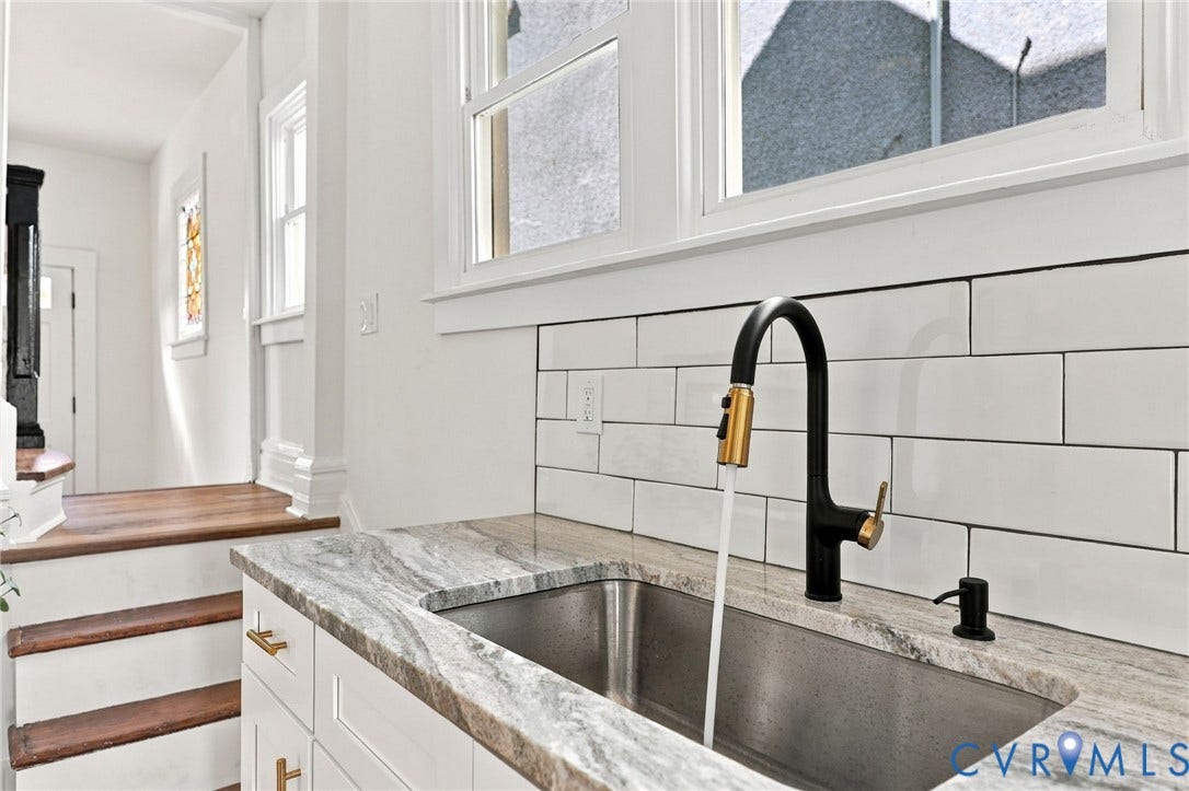 Kitchen featuring stone-patterned countertops, white rectangular tile backsplash, stainless steel undermount sink, and matte black high-arch pull-down faucet with brass accents