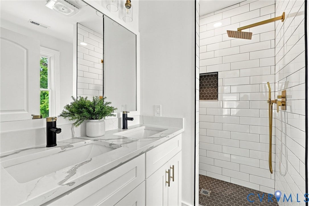 Double vanity with stone-patterned countertops and matte black faucets, paired with a walk-in shower featuring white subway wall tile, a brass rain-style showerhead, a handheld sprayer, and hexagonal floor tiling