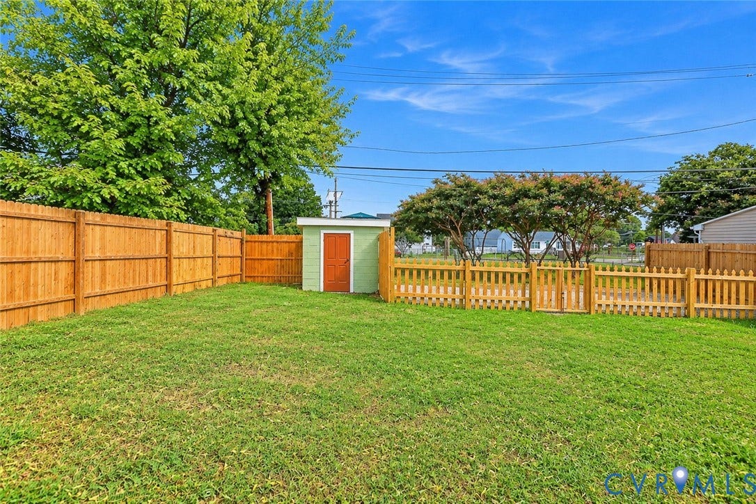 Backyard featuring a grass lawn, full-height perimeter wood fencing, a dedicated fenced-in area with a gate, and an exterior storage shed
