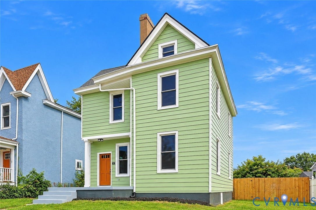 Two-story exterior featuring light green horizontal siding, a prominent gable roofline, a covered front porch with a supporting column, and a wood-tone entry door
