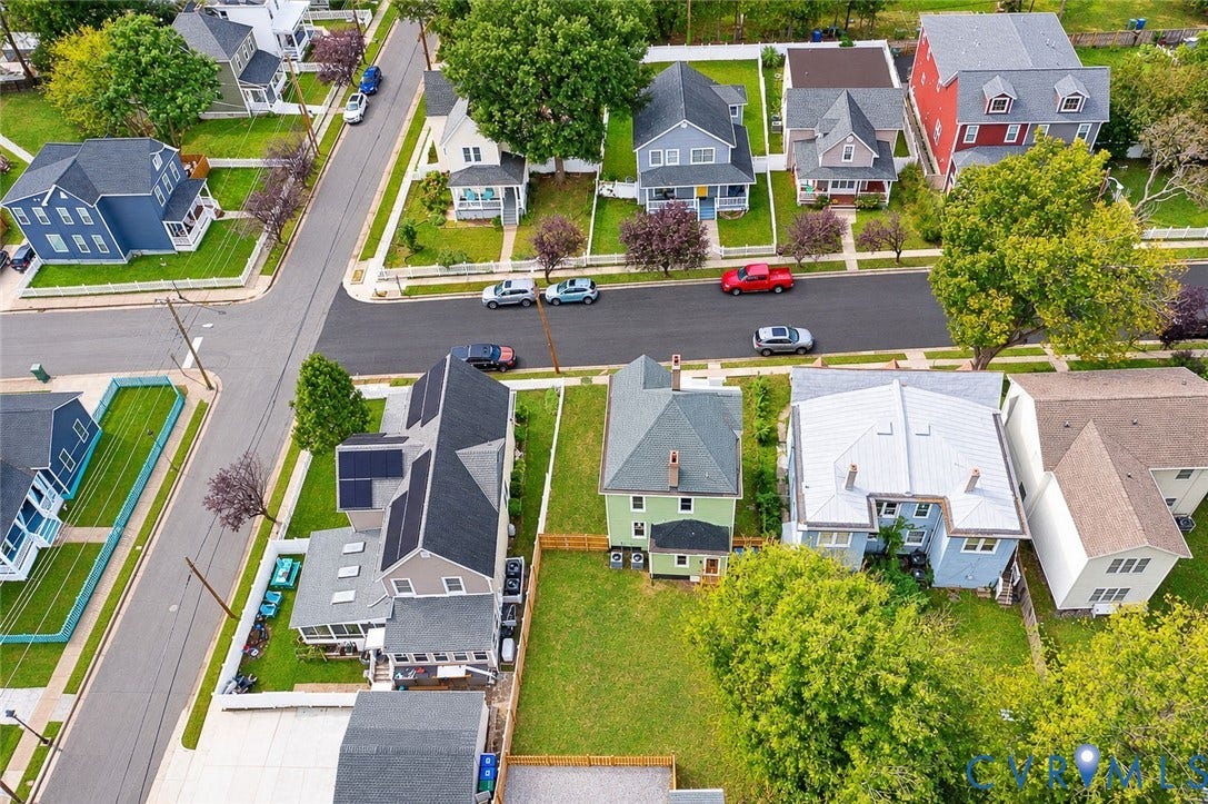 Aerial perspective of a multi-story residence featuring a pitched roof, integrated solar panels, private fenced rear yard, and detached garage