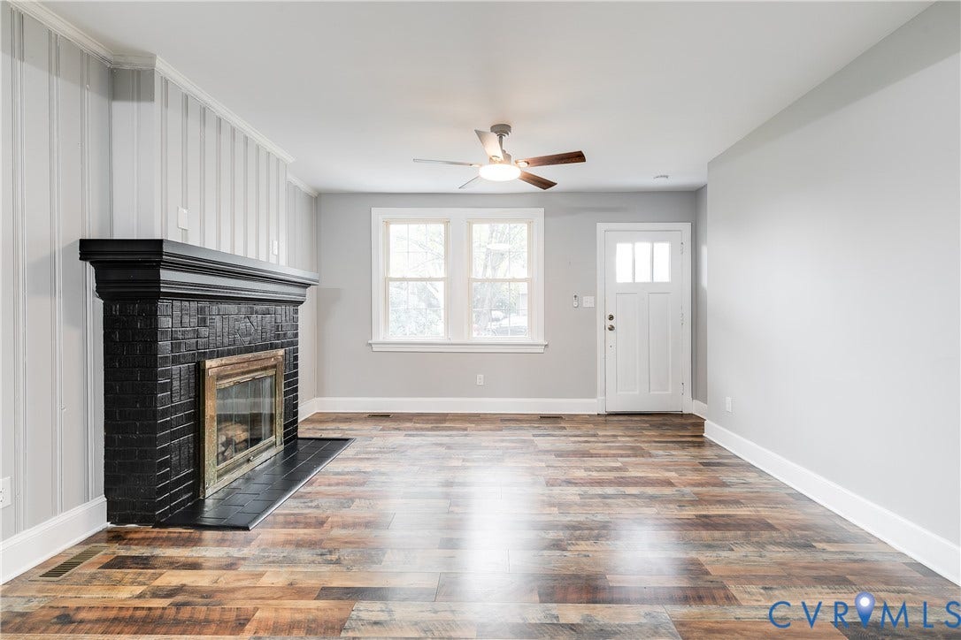 2012 Bailey Avenue, Richmond, VA 23231 Wood-finish flooring, black brick fireplace with mantel, ceiling fan with integrated lighting, multiple windows, and a panel door with transom-style lites