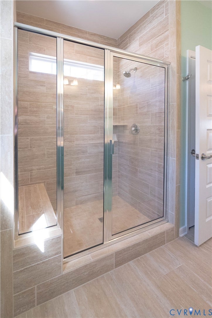 Shower enclosure with glass panels, a horizontal window, wall-mounted showerhead, built-in shelving, and an integrated bench