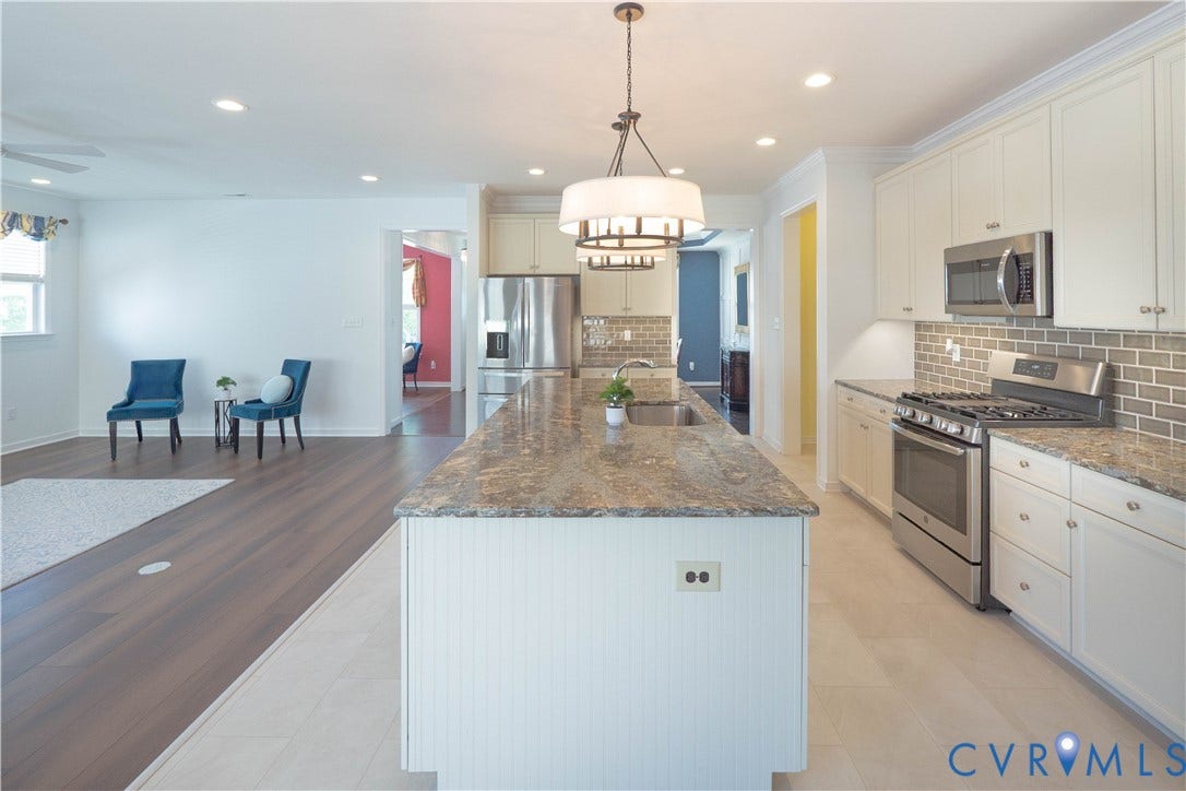 Kitchen island with an undermount sink, pendant lighting, stainless steel appliances, and subway tile backsplash