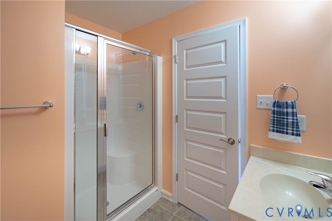 Walk-in shower with glass enclosure, single vanity with integrated sink, and paneled door