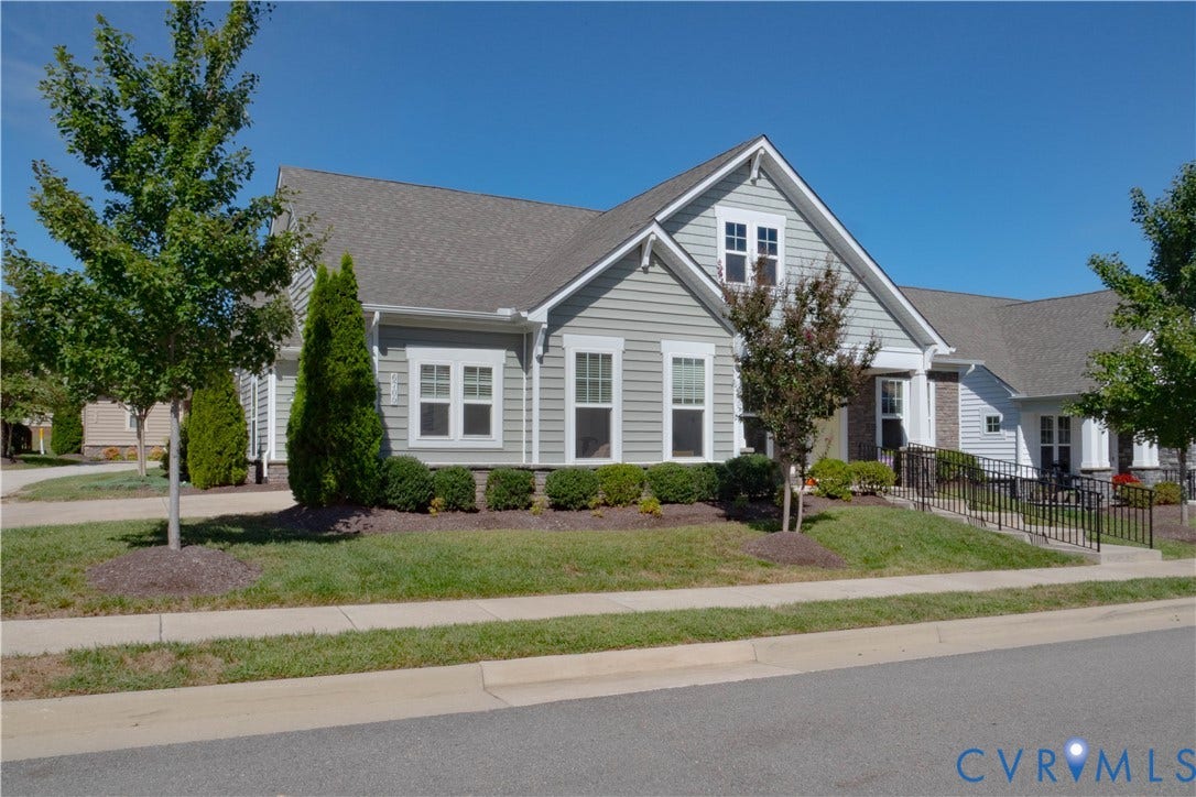 Light gray horizontal siding, pitched shingle roof, white trim windows, brick accents, and a black metal handrail