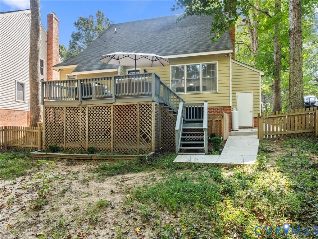 Upper-level deck with wood railing, lower-level lattice skirting, wood picket fencing, and a concrete ramp