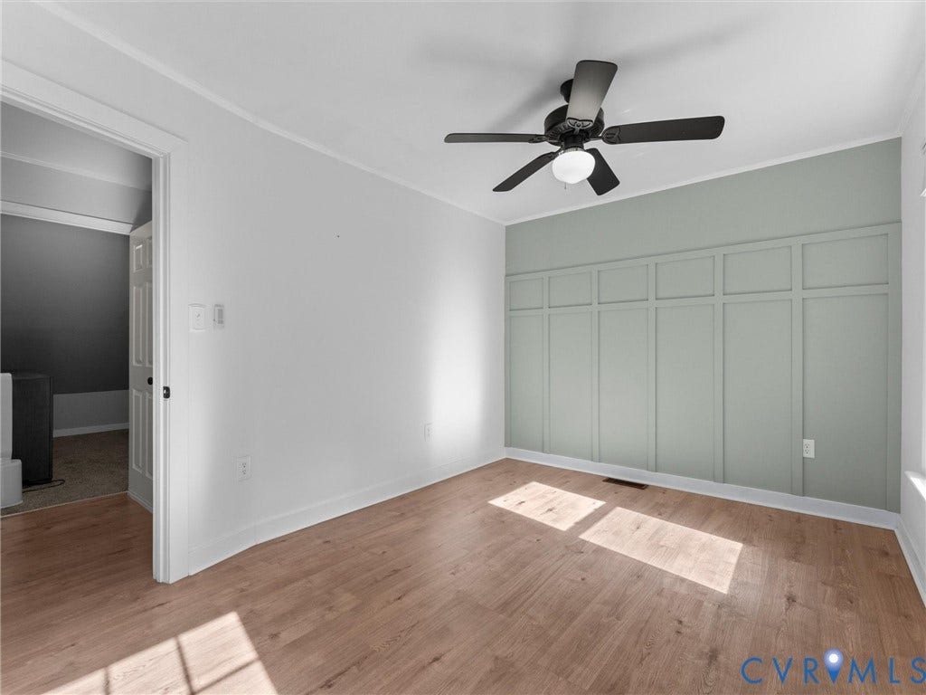 Wood-finish flooring, accent wall with decorative paneling, ceiling fan with integrated lighting, white trim