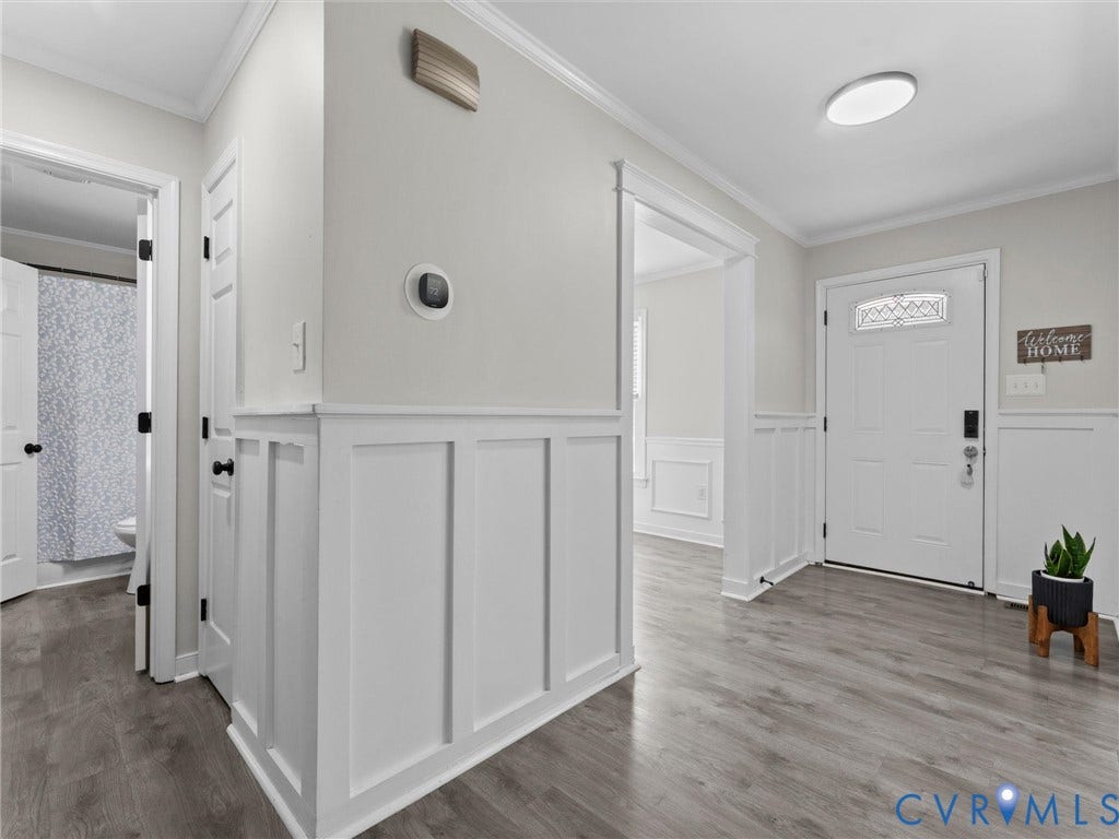Panel molding with crown molding accents, wood-finish flooring, and white interior doors with black hardware