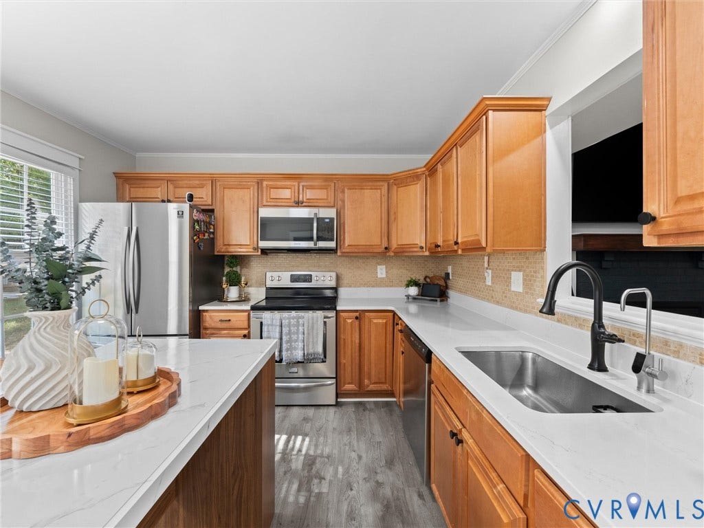 Kitchen with light-toned wood cabinetry, stainless steel appliances, a tile backsplash, and light-toned countertops