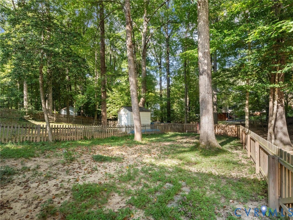 Expansive outdoor space featuring mature trees, a wooden picket fence, and a storage shed