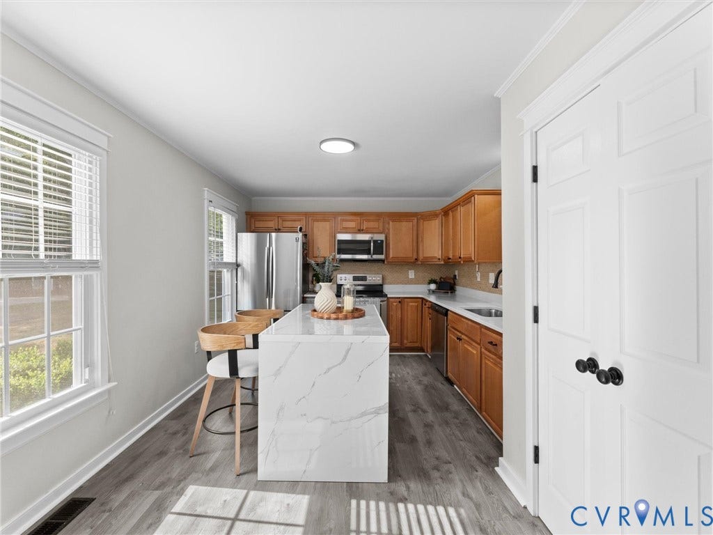 Kitchen featuring wood-finish flooring, a waterfall-edge island, recessed lighting, and stainless steel appliances