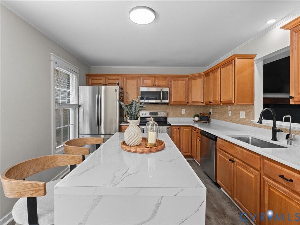 Kitchen featuring a waterfall island with stone-finish countertop, stainless steel appliances, wood-finish cabinetry, and a tile backsplash