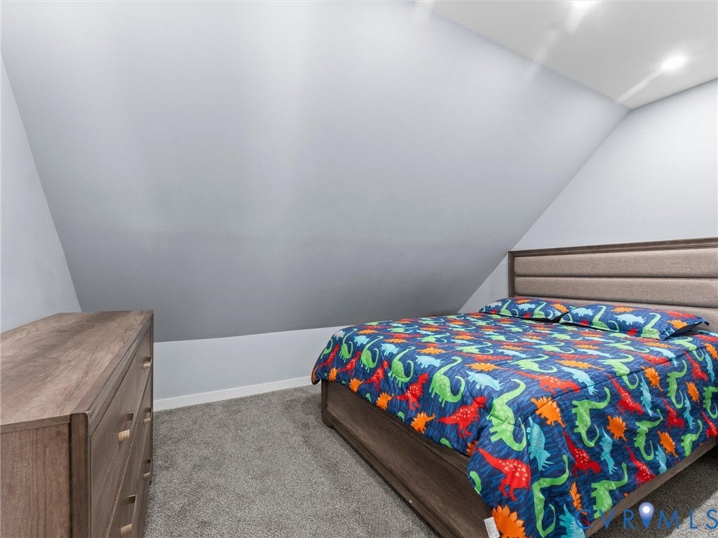 Sloped ceiling architecture with recessed lighting, plush grey carpeting, and a wood-finish bed frame with an upholstered headboard