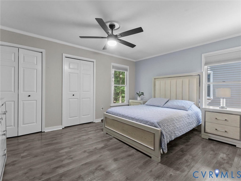 Wood-finish flooring, two windows, two white bi-fold closet doors, and a ceiling fan with integrated lighting