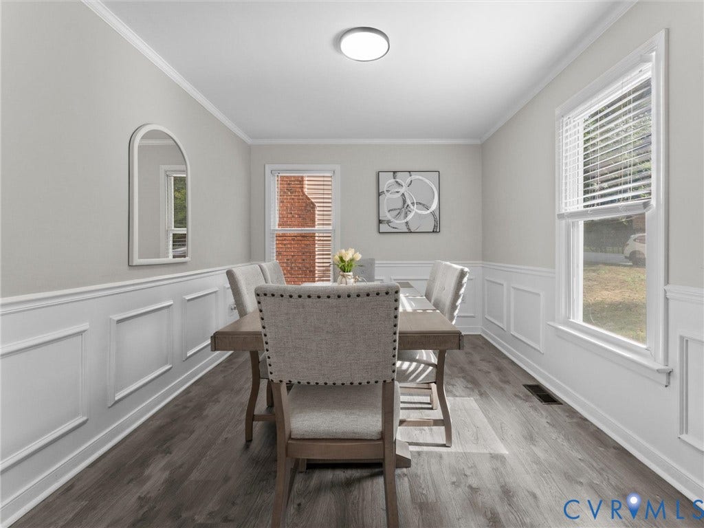 Recessed panel wainscoting, crown molding, wood-finish flooring, two large windows, and a flush-mount ceiling light