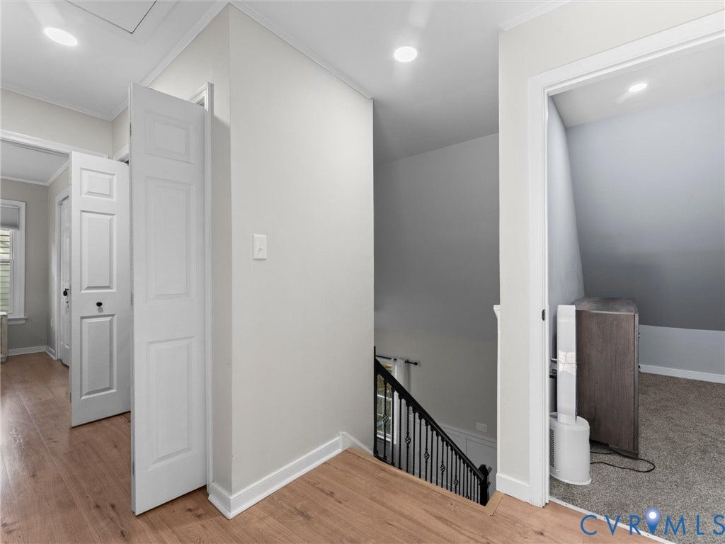 Wood-finish flooring leading to a staircase with a black wrought iron railing, white paneled doors, and recessed lighting