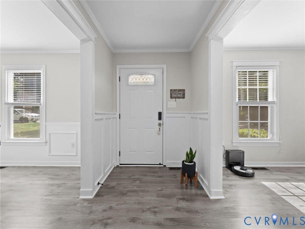 Entryway featuring wood-finish flooring, white paneling, and an entry door with decorative glass
