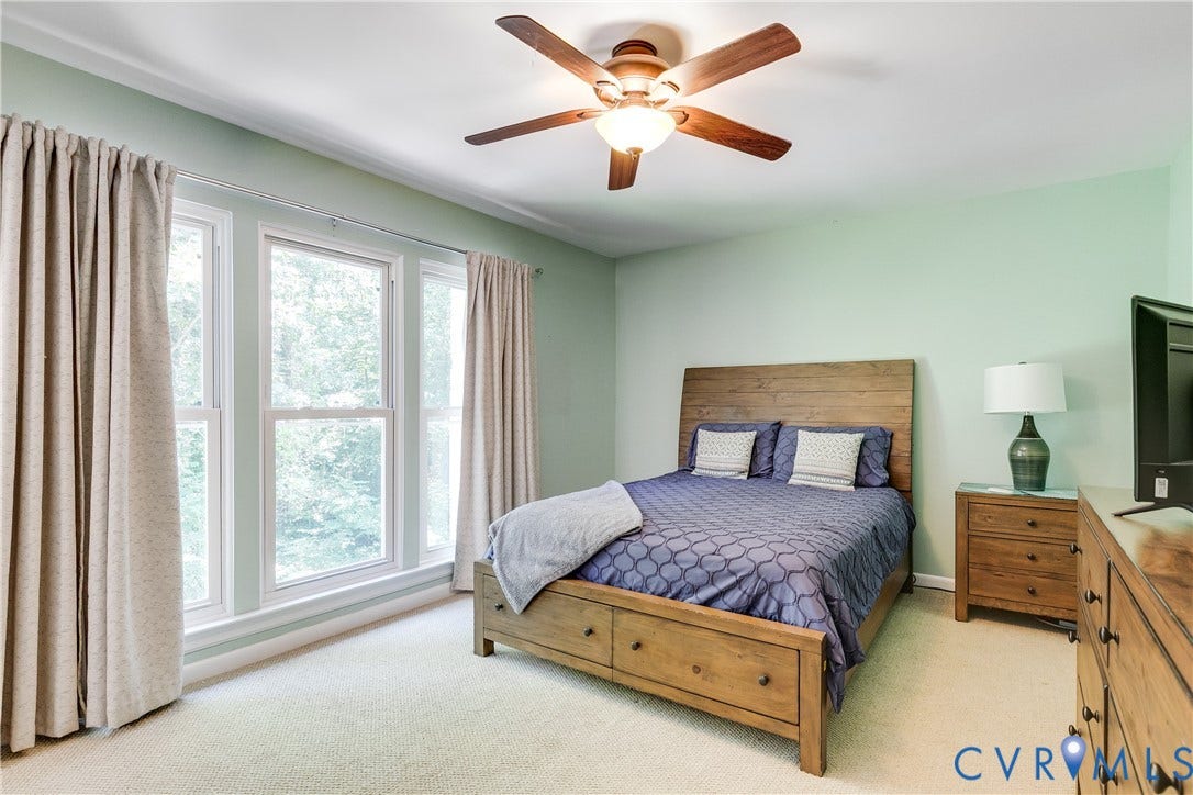 Triple window array with light-colored trim and neutral curtains, complemented by light green walls, a wood-finish ceiling fan, and light-colored carpeting