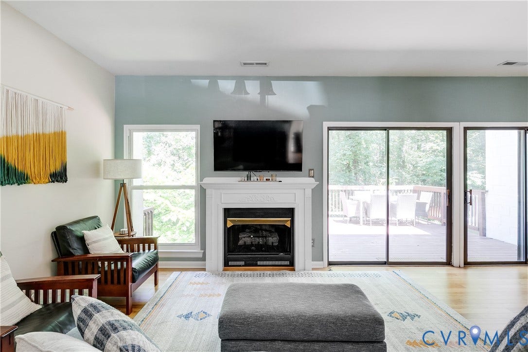 Living area featuring a fireplace with a white mantel, hardwood flooring, and multiple sliding glass doors opening to an exterior deck