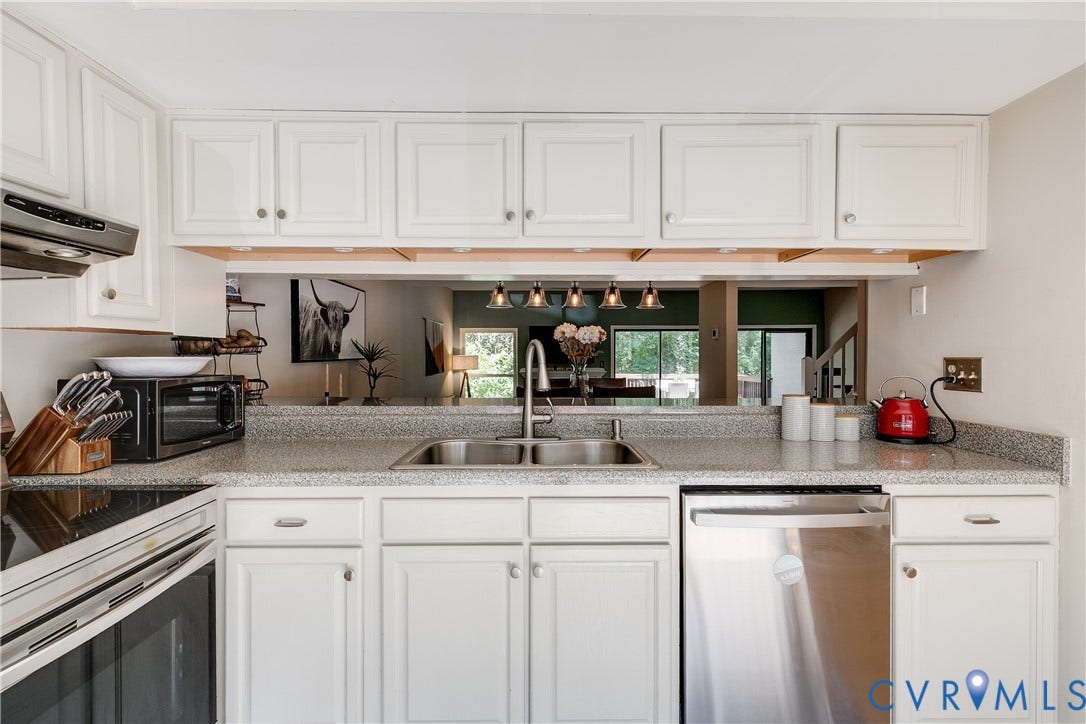 Kitchen featuring white cabinetry, a double basin stainless steel sink, a stainless steel dishwasher, a built-in range, and a pass-through window with pendant lighting