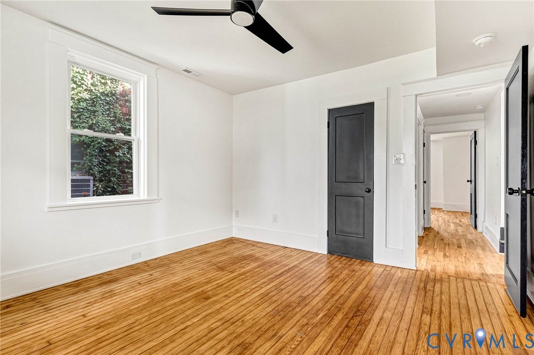 503 Pollock Street, Richmond, VA 23222 Hardwood flooring, white walls, black ceiling fan, window with exterior foliage, and a dark-paneled door