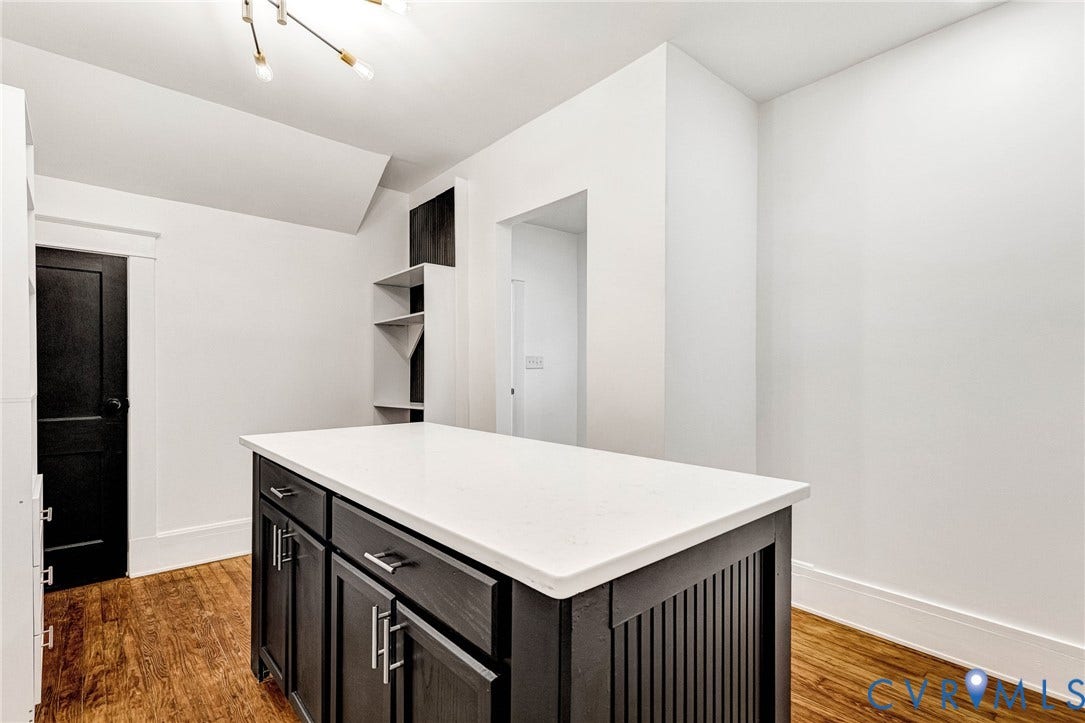 503 Pollock Street, Richmond, VA 23222 Central island with a white countertop and dark cabinetry, wood-finish flooring, built-in shelving, and a modern ceiling fixture