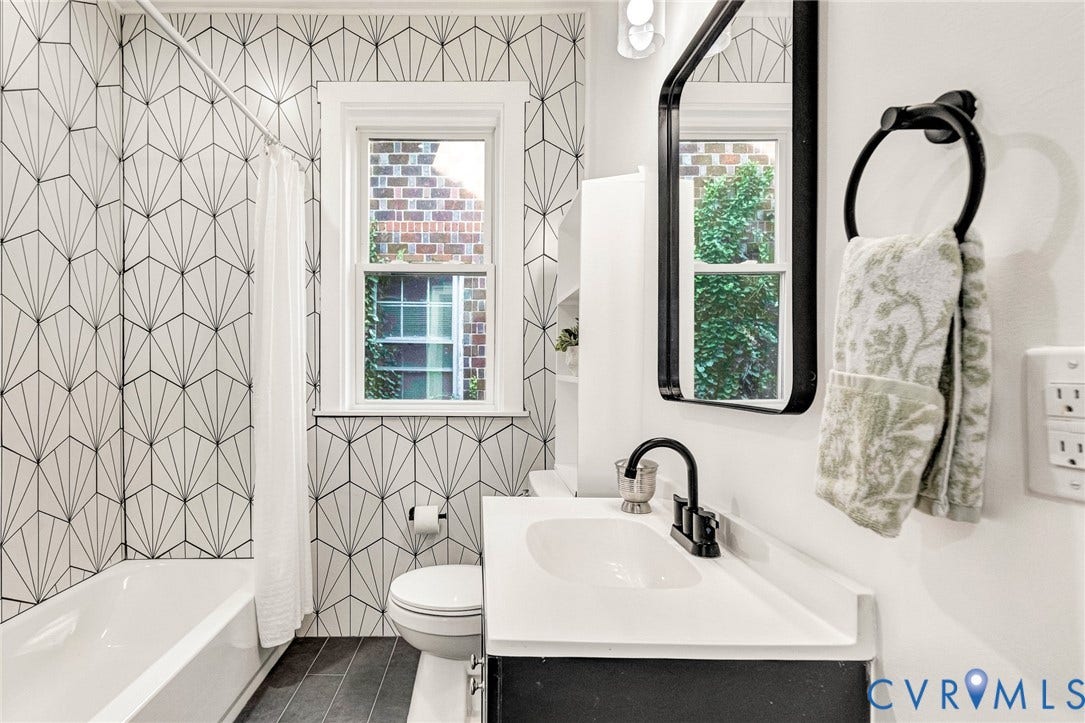 503 Pollock Street, Richmond, VA 23222 Bathroom featuring a white bathtub, a single vanity with a white countertop and dark cabinet, a black-framed mirror, and geometric pattern wall tile