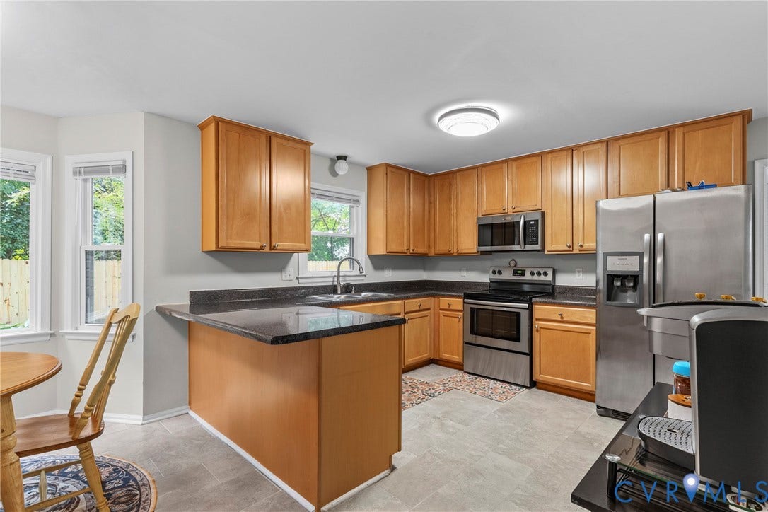 Kitchen featuring wood cabinetry, dark countertops, stainless steel appliances, and bay windows