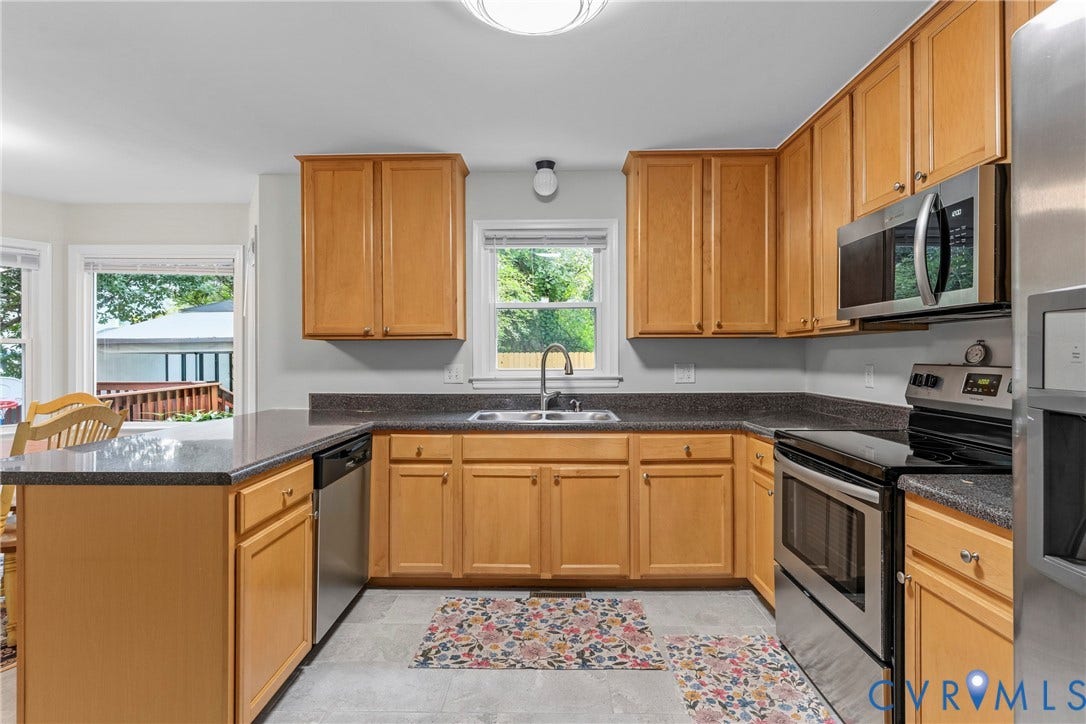 Kitchen featuring wood cabinetry, stainless steel appliances, dark countertops, and a double basin sink