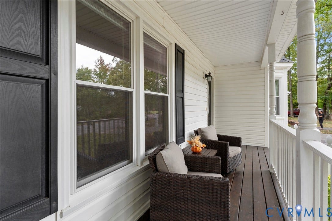 Covered front porch featuring white siding, dark wood-finish flooring, white railing, and decorative columns