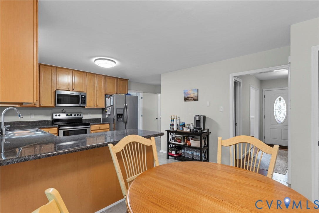 Kitchen featuring wood-finish cabinetry, stainless steel appliances, dark stone countertops, and an integrated sink with a high-arch faucet