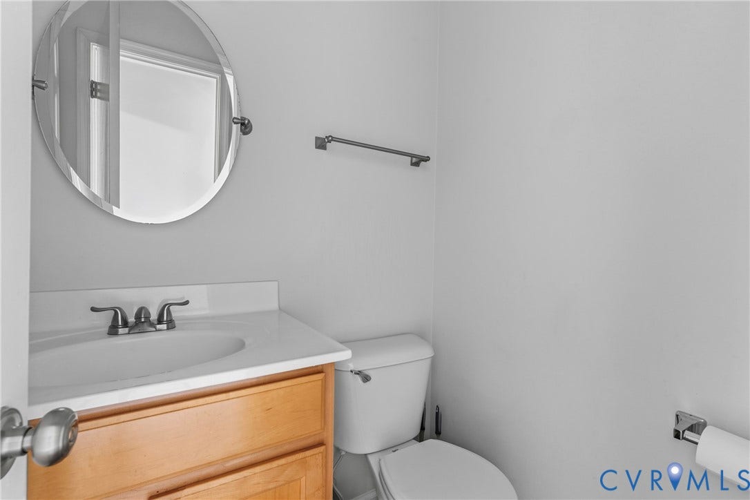 Wood-finish vanity with an integrated white sink and counter, chrome faucet, and oval mirror